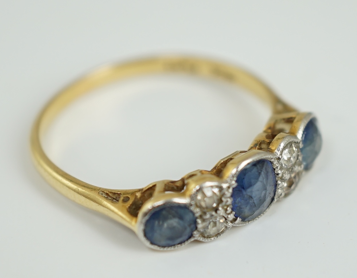 A 1920's 18ct gold and platinum, millegrain set three stone sapphire and four stone diamond half hoop ring